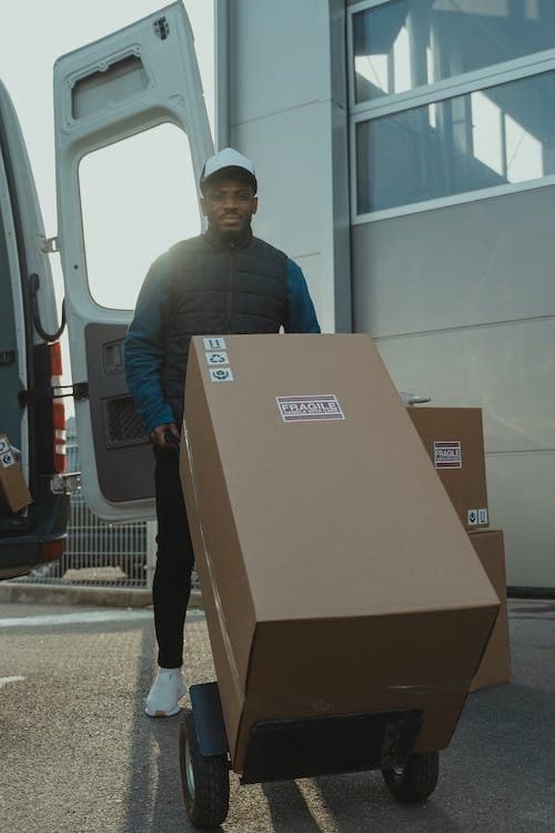 Delivery worker with a hand truck loaded with boxes next to a van.